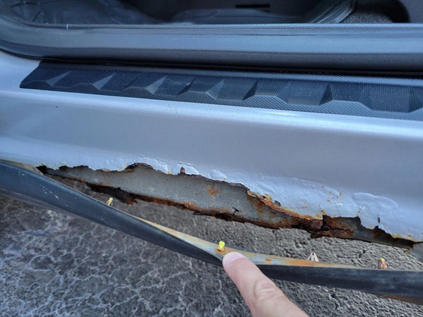 Rust damage on a car door with a hand holding a tool. Rusted Outer rocker panel. 